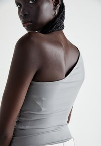Gray sleeveless top with a smooth, fitted design, featuring subtle ruching on the side and a rounded neckline, worn against a light background.