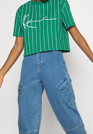 Green cropped t-shirt with white vertical stripes and a white graphic design. Paired with blue denim cargo pants featuring multiple pockets.