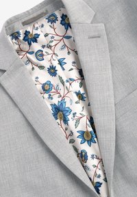Blazer grigio chiaro con una fodera floreale caratterizzata da fiori blu, foglie verdi e dettagli rossi, realizzato in un tessuto liscio con una texture raffinata.