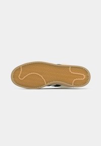 Sneaker outsole featuring a herringbone pattern, beige rubber with a textured surface, and black accents along the side.