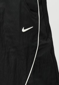 Μαύρο ύφασμα με λευκή καμπυλωτή επένδυση και λευκό λογότυπο Nike Swoosh κοντά στο άνοιγμα της τσέπης στη δεξιά πλευρά.