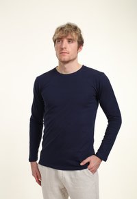 Marinblå långärmad tshirt i mjukt tyg, med rund halsringning och en kroppsnära design. Kombinerad med ljusa byxor.