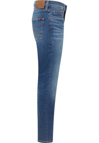 Dżinsy męskie o dopasowanym kroju w średnim odcieniu niebieskiego. Posiadają pięć kieszeni, skórzaną naszywkę na pasku oraz kontrastowe przeszycia na tylnych kieszeniach.