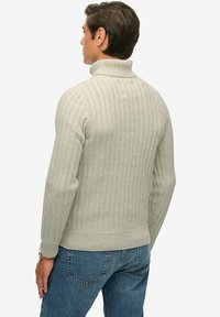 Szary sweter z golfem o prążkowanej strukturze, z dopasowanymi rękawami i szerokim kołnierzem, w połączeniu z niebieskimi dżinsami.