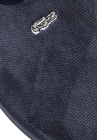 Zapatilla de color azul oscuro con parte superior de tela texturizada, forma redonda y un pequeño logo bordado en blanco en el exterior. Suela de goma visible.