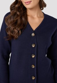 Cardigan lavorato a maglia blu navy con scollo a V, cinque grandi bottoni rotondi di tonalità contrastanti e orlo a costine per un tocco di consistenza.