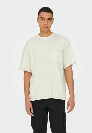 Cremefarvet oversized t-shirt lavet af bomuld, med en brystlomme og kontrastfarvet sort syning, stylede med sorte cargo bukser.