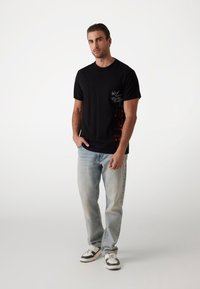 Sort bomulds T-shirt med korte ærmer, prydet med tekstgrafik og farverigt sideskærm, parret med lyseblå afslappede jeans og sneakers.