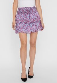 Světle modrá sukně s volány vyrobená z průhledné látky s červenými květinovými vzory. Sukně má nařasený pas a vrstvené volány, v kombinaci s černými vysokými podpatky.