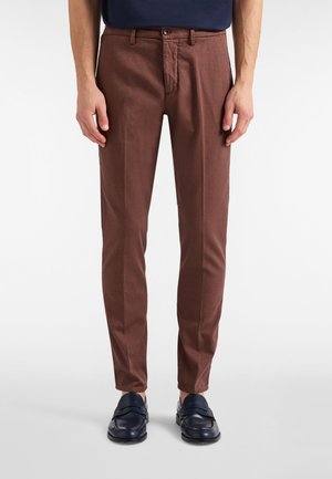 Brune skræddersyede bukser med tekstureret stof, slank pasform og diskrete nålestriber; har en lynlås foran og knaplukning. Bæres med marineblå loafers.