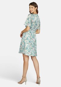 Blumenkleid in Hellblau mit kurzen, flatterhaften Ärmeln. Hat eine taillierte Taille und einen weit ausgestellten Rock, geschmückt mit mehrfarbigen Blumen und Blättern.