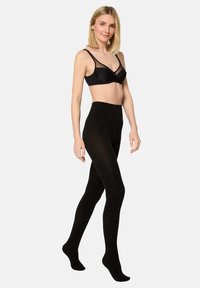 Tights negros opacos con una textura suave, diseño de cintura alta y una silueta ajustada, exhibidos en un modelo con un sujetador negro a juego.