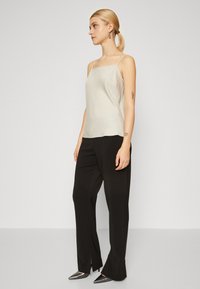Light beige satin camisole with thin straps, paired with black trousers featuring side slits and pointed metallic heels. Simple design overall.