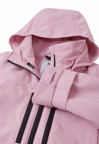 Giacca impermeabile rosa con cappuccio; presenta cerniere nere, bottoni a pressione e una superficie opaca liscia. Dettaglio: doppie strisce nere sulla parte anteriore.