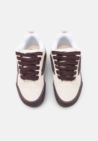 Paire de baskets beige et marron foncé avec doublure intérieure blanche et lacets marron foncé, vues de dessus sur fond blanc.