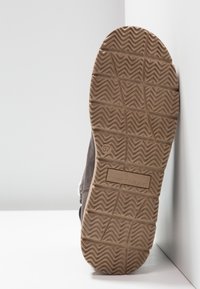 Pohja ruskeasta kengästä, jonka urat ovat sahalaitaista kuviota, koko 37, ja Tom Tailor -brändin nimi painettuna pohjaan.