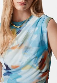 Helleblaues Oberteil mit floralem Muster, das orangefarbene und gelbe Akzente aufweist, aus drapiertem Stoff und mit einem runden Ausschnitt. Goldene Kettenhalskette ist im Lieferumfang enthalten.