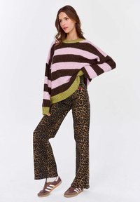 Gruby sweter w różowo-brązowe paski, połączony z rozszerzającymi się spodniami w leopardzy wzór. Sneakery w brązowo-białe paski dopełniają całość.