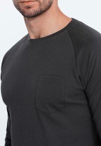 Pitkähiha, tummanharmaa paita, jossa on ribbitekstuuri. Siinä on paikalla vasemmalla rinnassa ja pyöreä kaula-aukko.