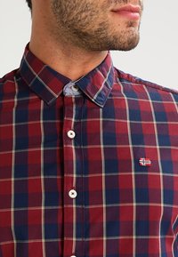 Rot-blau kariertes Hemd mit Button-Down-Kragen, weißen Knöpfen und einer kleinen, auf der Brust gestickten norwegischen Flagge.