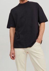 Svart bomullströja med korta ärmar och rundad halsringning, kombinerad med ljusa, åtsittande byxor. Tyget ser slätt och utan struktur ut.