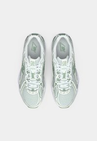Valge ja rohelise värviga New Balance jooksujalatsite paar, vaadetuna pealtpoolt, helehalli tausta peal.