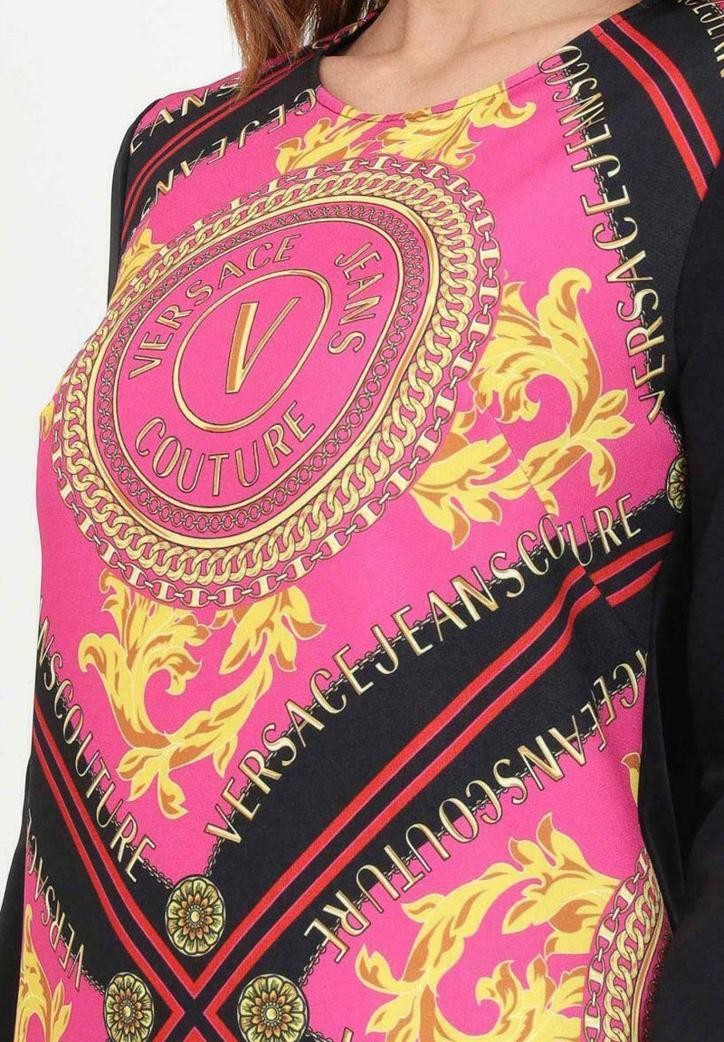 Versace-Oberteil mit einem rosa, schwarzen und goldenen Muster, das reichhaltige Details, Logotext und Kettenmotive zeigt. Weicher, glatter Stoff; kurze Ärmel.