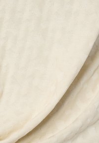 Tejido de punto color crema con un sutil patrón geométrico y suaves pliegues que crean sombras delicadas.