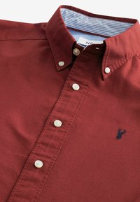Chemise boutonnée coloris bordeaux dotée d'un col classique, de boutons nacrés et d'un col intérieur à rayures bleues. Comprend un petit logo marine sur la poitrine.