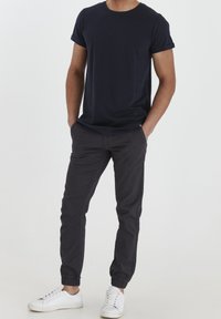 Laivastonsininen pyöreäkauluksinen t-paita, lyhyet hihat, yhdistetty tummanharmaisiin joggityylisiin housuihin ja valkoisiin tennareihin, joissa on nauhakuviot ja kumipohjat.