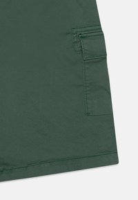 Pantaloni corti in tessuto verde scuro con tasca laterale, orlo piatto e una texture sottile. Presentano cuciture rinforzate e una finitura liscia.