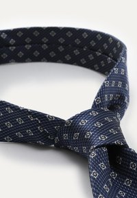 Dunkelblauer Krawatte mit strukturiertem Muster aus kleinen Rauten in Silber. Hergestellt aus gewebtem Stoff, hat sie einen Standard-Krawattenknoten.