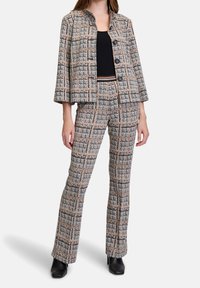 Tweed kostymset som har en kort jacka med runda knappar och matchande utsvängda byxor i ett svart, beige och grått rutig mönster.