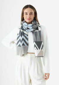Écharpe à motifs en gris, blanc et bleu clair. Présente des designs géométriques, une texture lisse et des bords frangés. Portée lâchement autour du cou.