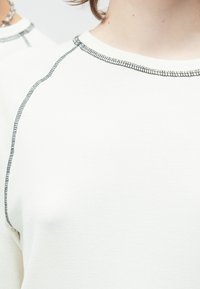 Valge pika varrukaga särk tekstuurse kangaga. Kaeluse ja õmbluse servades kontrastne must õmblus.