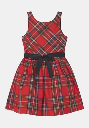 Czerwona sukienka w kratę bez rękawów, z czarnymi, żółtymi i białymi liniami, podkreślona w talii czarnym paskiem zawiązanym na kokardę.
