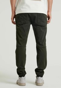 Mörkgröna cargobyxor med en tapered passform, två stora bakfickor och elastiska cuffs. Bärs med ljusgrå sneakers.