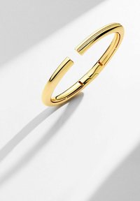 Guldpläterat armband med en minimalistisk, öppen design som har släta kurvor och en texturerad, rak kant.