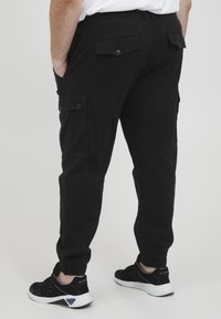 Schwarze Cargo-Hosen mit Seitentaschen, elastischen Bündchen und geknöpften Gesäßtaschen. Der Stoff hat eine glatte Textur und eine lockere Passform.