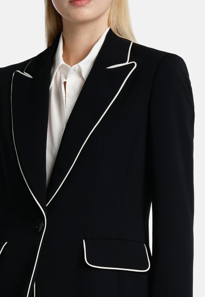 Blazer blu navy con piping bianco, chiusura con un bottone e due tasche frontali. Fit sartoriale, realizzato in tessuto liscio.