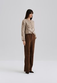 Cardigan lavorato a maglia beige con motivi zigzag marroni, dotato di tre bottoni dorati; abbinato a pantaloni larghi in suede marrone a vita alta.
