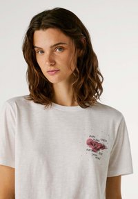 T-shirt en coton blanc avec un graphique sur le devant d'un cœur rose avec des ailes et le texte "Pepe Jeans London Portobello Road Denim Brand."
