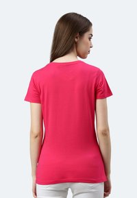 T-shirt aderente in cotone rosa con maniche corte, scollatura rotonda e texture liscia. La vista posteriore mostra un orlo leggermente curvo.