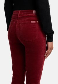 Rode corduroy broek met een lichte glans, vijf-pocket ontwerp en gestikte achterzakken. Label zichtbaar nabij de tailleband aan de achterkant.
