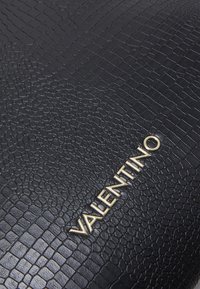 Černá strukturovaná kožená taška s krokodýlím vzorem a zlatým logem "VALENTINO". Vyznačuje se hladkým povrchem a pevným designem.