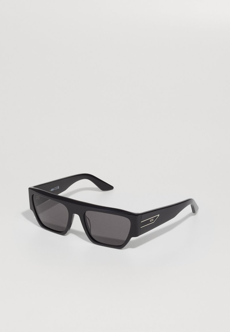 Ochelari de soare negri cu un cadru rectangular, lentile întunecate, finisaj mat și accente argintii pe brațe. Brațe texturate pentru aderență.