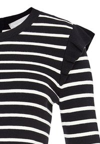 Randig svart-och-vit tröja med ribbat mönster, med rundad hals och volangdetaljer på axlarna.