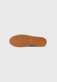 Rubber shoe sole with a textured, honeycomb pattern. Orange color, featuring the word "CONVERSE" embossed on a rectangular section.