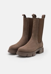 Bottines en daim marron à panneaux élastiques sur les côtés, bout rond et semelles en caoutchouc épaisses. Comprend des languettes pour un enfilage facile.