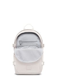 Sac à dos gris clair en tissu avec une forme arrondie, présentant un rabat, des poches zippées et une étiquette de logo à l'avant.